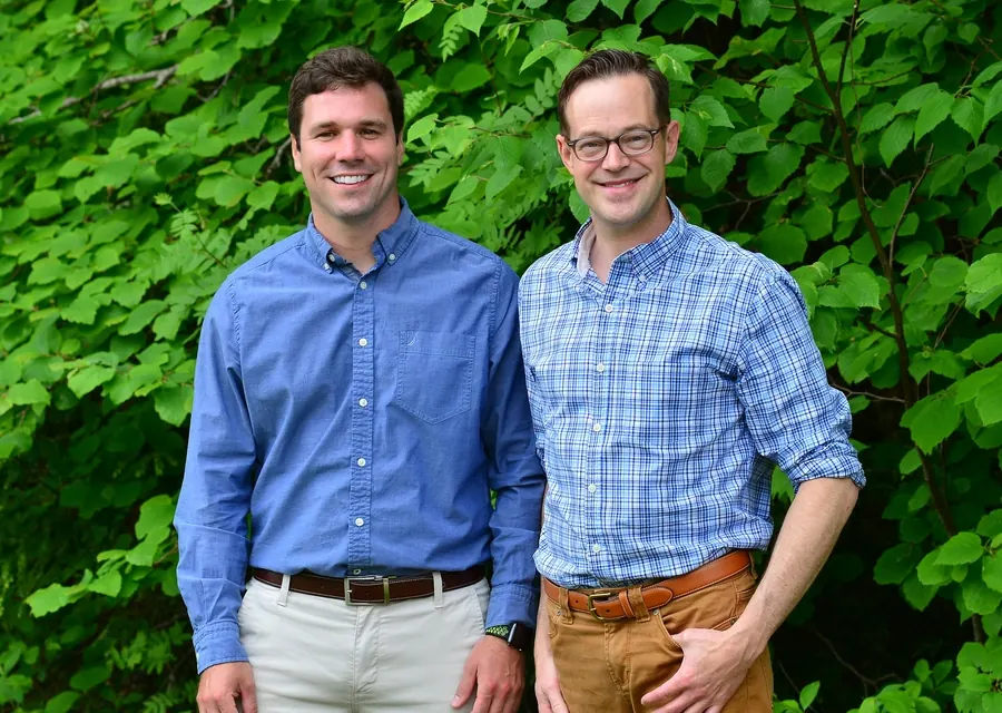 Dr. Darren Smith and Dr. Blair VanNostrand outdoors in front of green leaves.