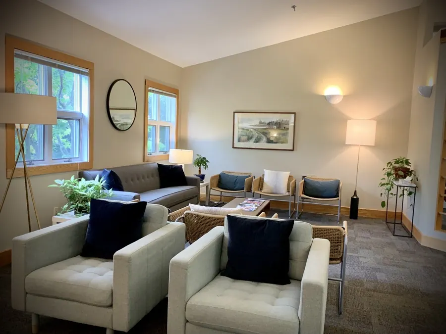 The waiting room at Falmouth Dental Health, with armchairs, a sofa and tall windows.